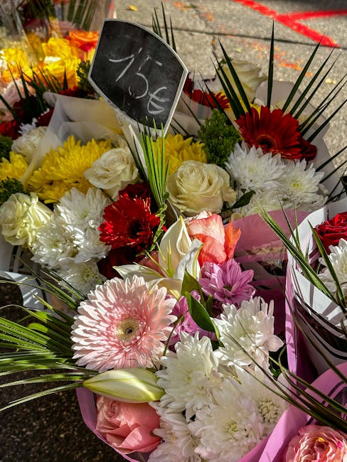 A vibrant floral arrangement featuring a variety of fresh flowers including white roses, pink gerbera daisies, red gerbera daisies, and white chrysanthemums, accented with long green leaves and blades