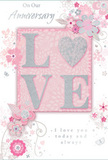 This romantic anniversary card is designed with the same attention to detail you might expect from a bespoke arrangement created in Earlsfield. At its centre, the word LOVE stands out in raised, block capitals, their surfaces layered with fine glitter that blends blush pink, pearly white, and a whisper of silver. The sparkle is soft and refined, reminiscent of the gentle sheen on newly opened rose petals in a florist's display along Garratt Lane. Encircling the central word is a flowing composition of stylised flowers and trailing leaves, drawn with delicate line work that suggests both care and spontaneity. The blossoms are coloured in muted tones of pastel pink and creamy ivory, with hints of grey and silver foil adding a subtle shimmer, much like light touching the leaves of a fresh bouquet. These floral motifs rest on a pale pink background that feels smooth and even, giving the card an overall sense of calm, intimate warmth, like a quiet evening at home near King George's Park. Interspersed among the flowers are tiny decorative curls, dots, and wisps that create a gentle sense of movement, as though the design is quietly breathing. Near the bottom, or slightly off to one side, flows an elegant anniversary message in soft grey script, speaking of lasting devotion, gratitude, and shared memories. The card's composition, with its mix of tactile texture and delicate illustration, makes it the perfect companion to a fresh arrangement delivered across Earlsfield and the surrounding SW18 area, a tender keepsake that celebrates enduring romance with understated grace.